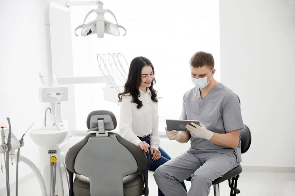 A dentist in scrubs and mask shows a tablet to a seated woman in a dental clinic with modern equipment in Tallahassee