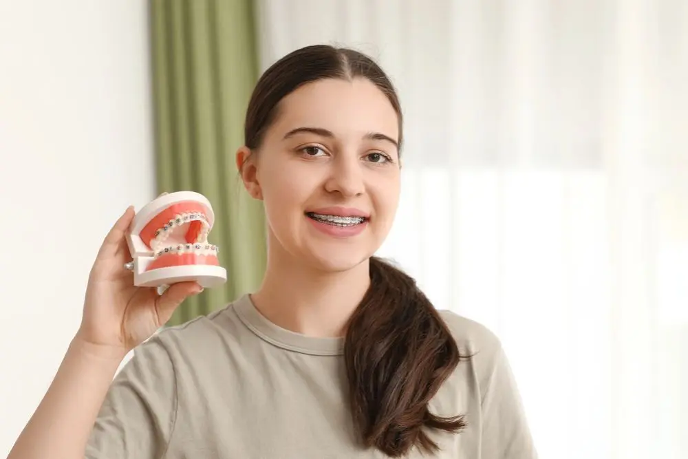 An adult smiles warmly, showcasing a dental model adorned with adult braces from Redemption Orthodontics in Tallahassee, FL.