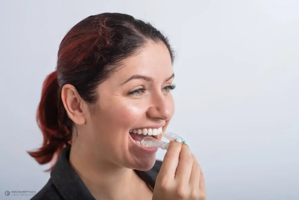 A person smiling while holding a clear dental aligner near their mouth, as one of the alternatives to braces in tallahassee, fl.