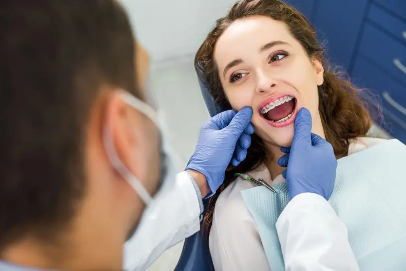 A woman with braces sitting in a dental chair while a dentist wearing gloves examines her adult braces at Redemption Orthodontics in Tallahassee, FL