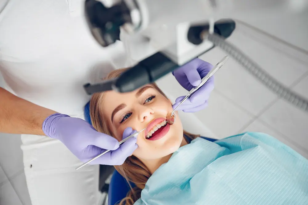A dentist wearing purple gloves examines a woman's teeth using dental tools while she lies in a dental chair with a blue bib as an example to show how to fix overbite in Tallahassee, FL.
