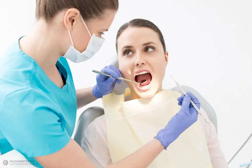 A dentist wearing gloves and a mask examines a woman’s open mouth with dental tools in a brightly lit clinic to show her how to fix overbite in Tallahassee, FL.