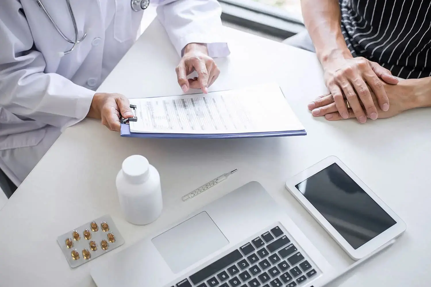 At Redemption Orthodontics in Tallahassee, FL, a doctor reviews a document invisalign insurance with a patient at a desk equipped with a laptop, tablet, medication, and thermometer.