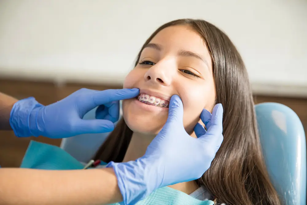 At Redemption Orthodontics' braces for overbite in Tallahassee, FL, a dentist in blue gloves examines a young girl's braces during her dental checkup.