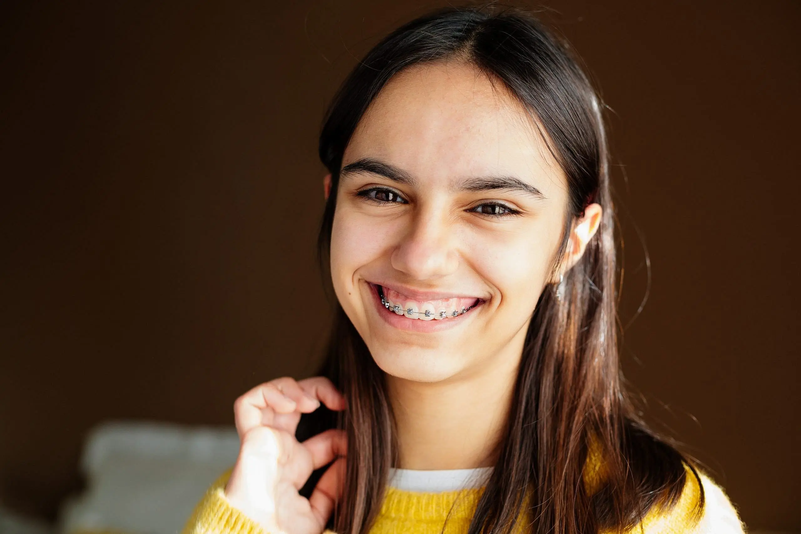 Smiling teen girl with long dark hair and braces at Redemption Orthodontics in Tallahassee, FL, wearing a yellow sweater.