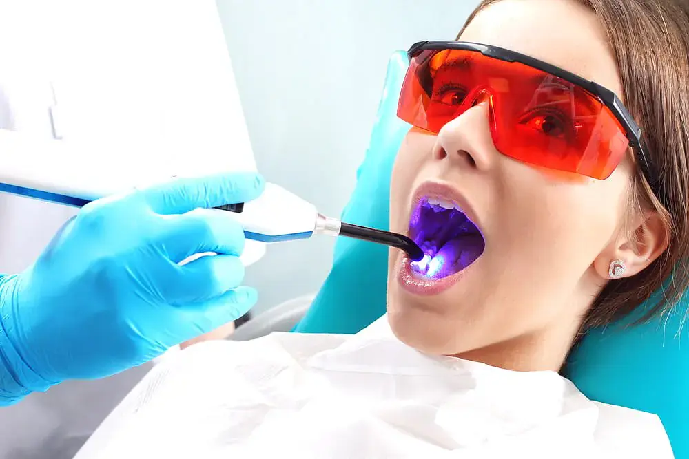 At Redemption Orthodontics in Tallahassee, FL, a dentist uses a curing light on a patient wearing red protective glasses after consider Invisalign vs Braces for dental treatment. At Redemption Orthodontics in Tallahassee, FL, a dentist uses a curing light on a patient wearing red protective glasses after consider Invisalign vs Braces for dental treatment.