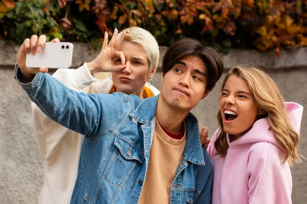 Three friends taking a selfie outside, one making a hand gesture, another looking amused while discussing different types of braces, and the third smiling widely in Tallahassee, FL.