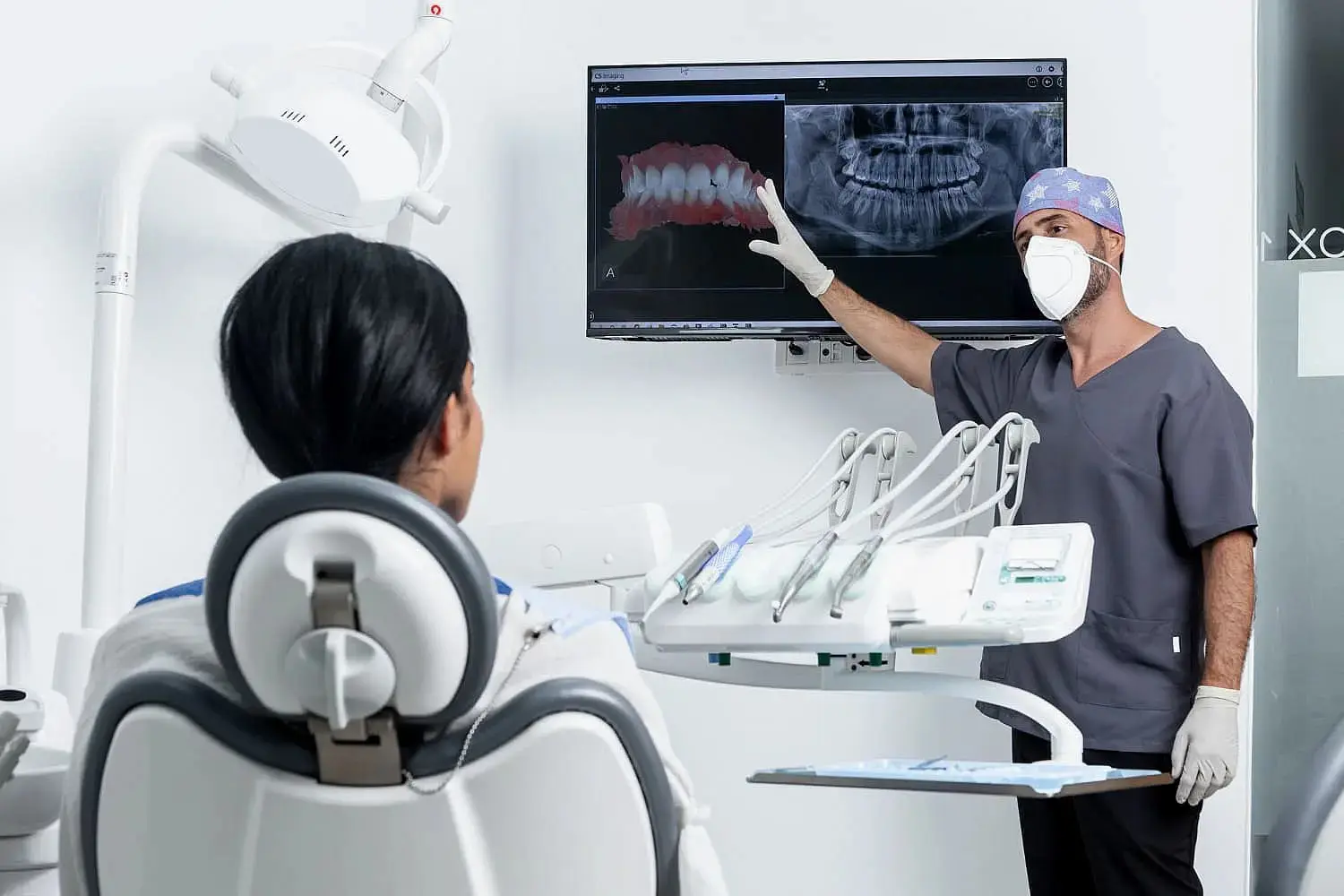 At Redemption Orthodontics in Tallahassee, FL, a dentist in scrubs and mask reviews dental X-rays about future advancements in jaw surgery with a patient in the chair.