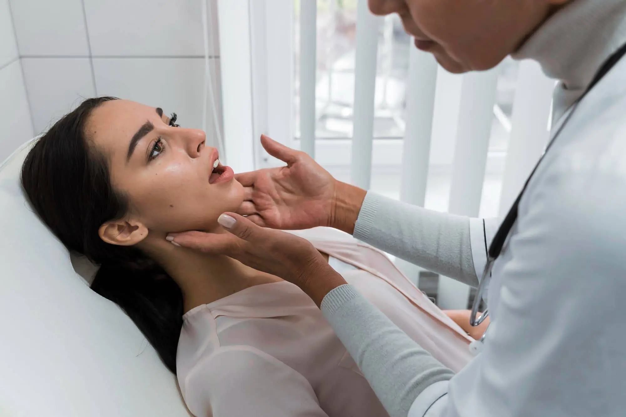 At Redemption Orthodontics in Tallahassee, FL, a doctor checks a woman's throat and jaw as she sits in a medical chair for rehabilitation exercises after jaw surgery.