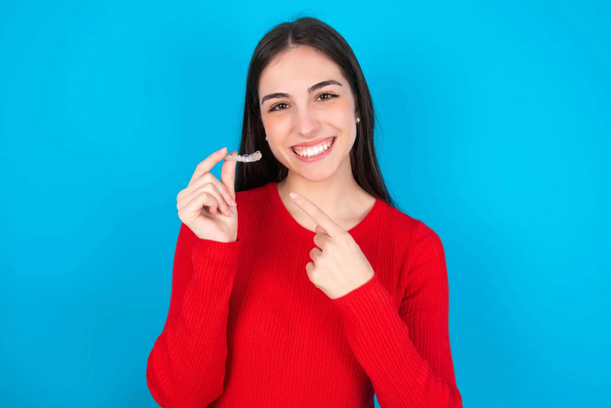 Smiling woman in a red sweater points to a Invisalign® Clear Aligners, with Redemption Orthodontics in Tallahassee, FL against blue backdrop.