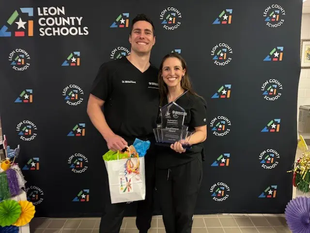 In Tallahassee, FL, Redemption Orthodontics representatives stand by a Leon County Schools backdrop with an award and gift bag.