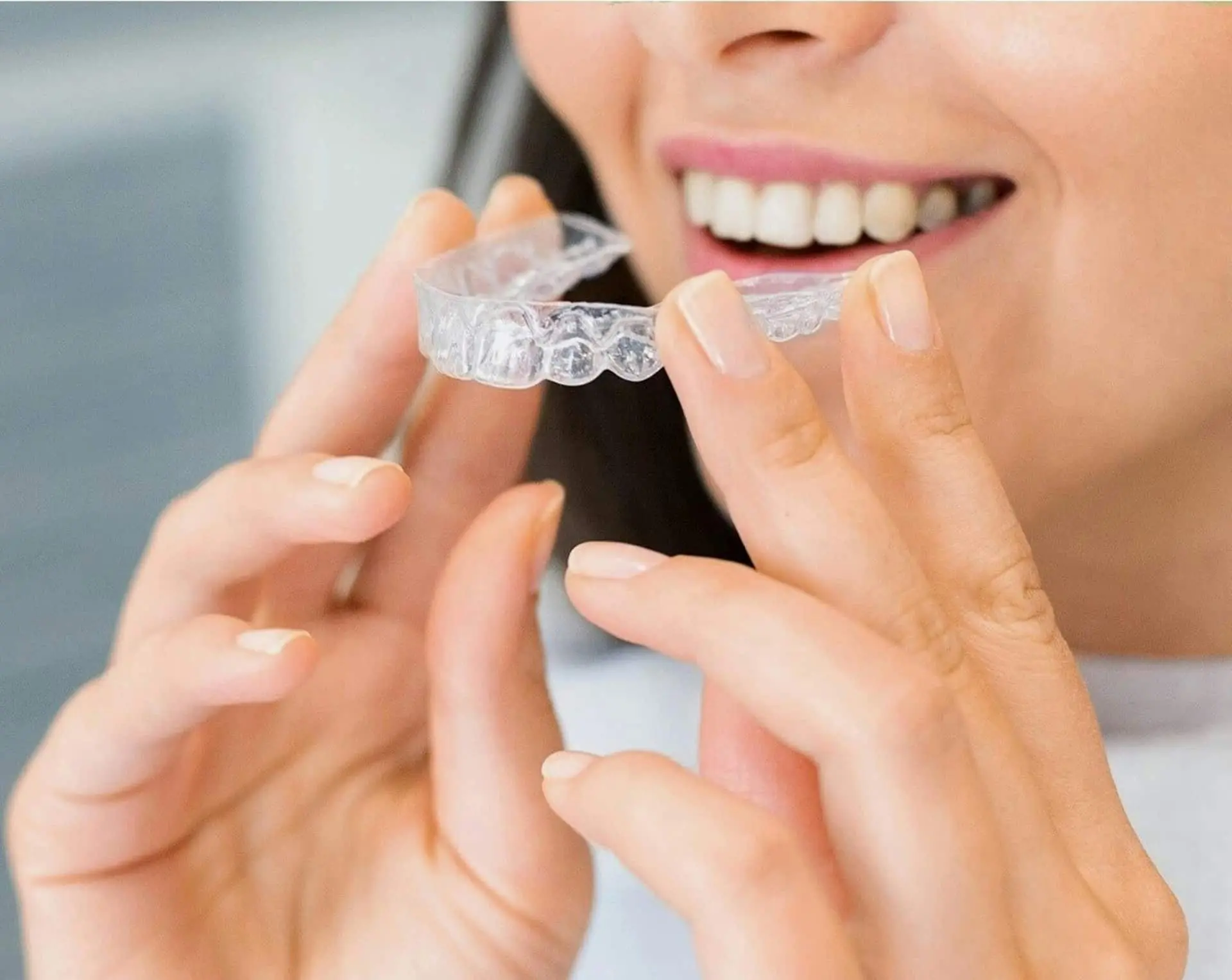 Smiling confidently with straight teeth, a person displays an Invisalign aligner from Redemption Orthodontics in Tallahassee, FL.