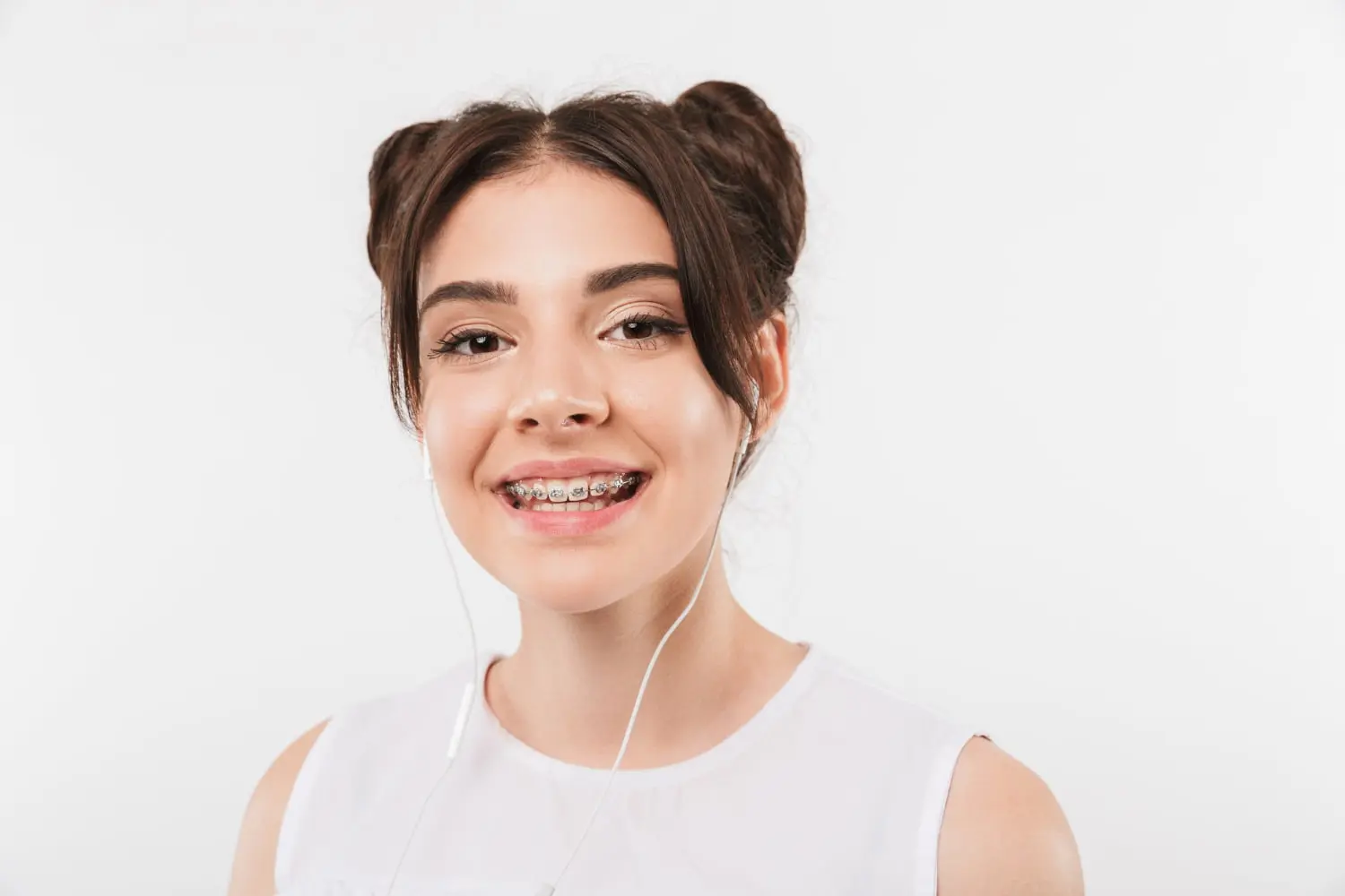 Smiling teen with braces listens to music at Redemption Orthodontics in Tallahassee, FL; brown hair in double buns, white top.