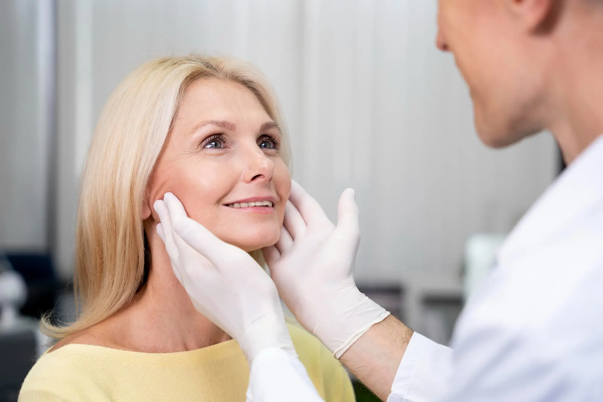 In Tallahassee, FL, a doctor at Redemption Orthodontics examines a smiling woman’s jawline to assess her for jaw surgery.