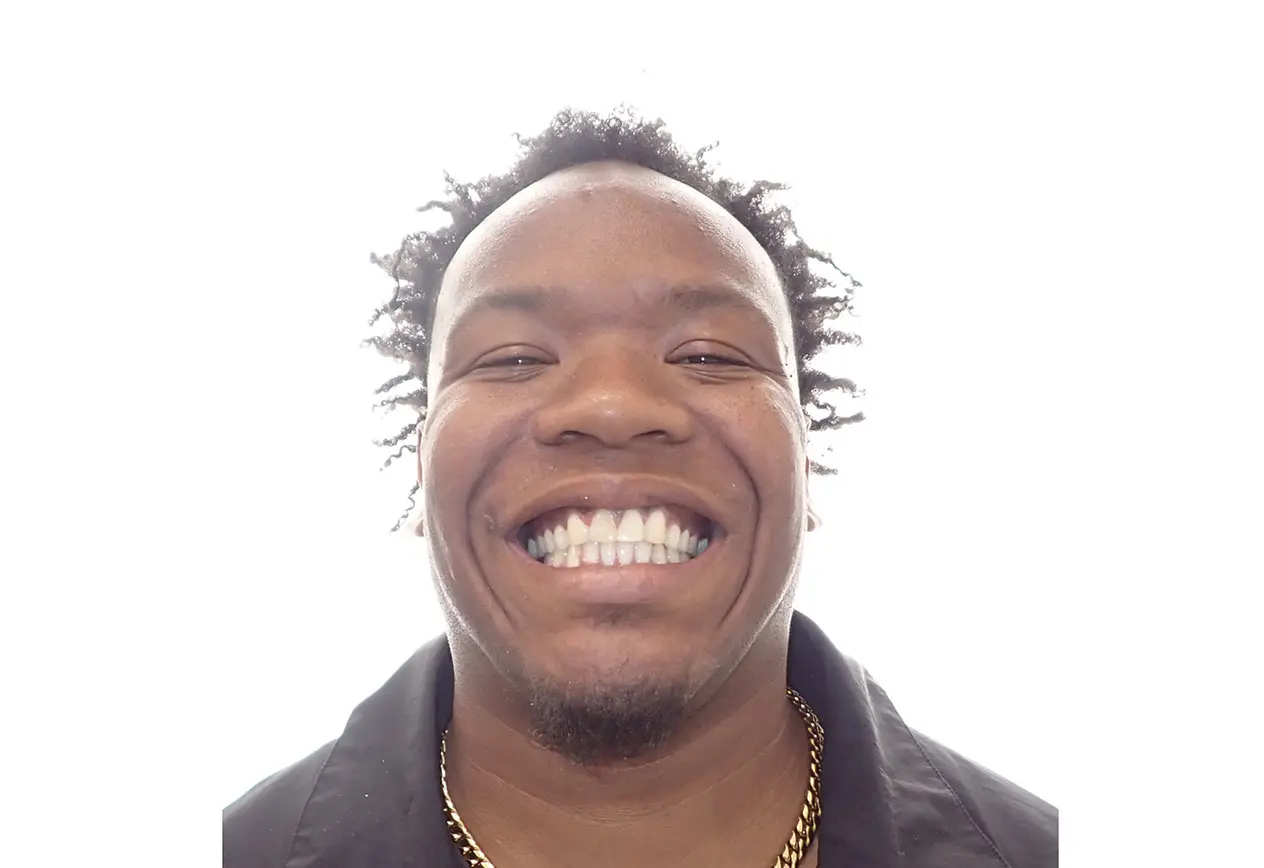 Smiling after braces at Redemption Orthodontics in Tallahassee, FL, a person with curly hair and goatee wears black jacket and gold chain.