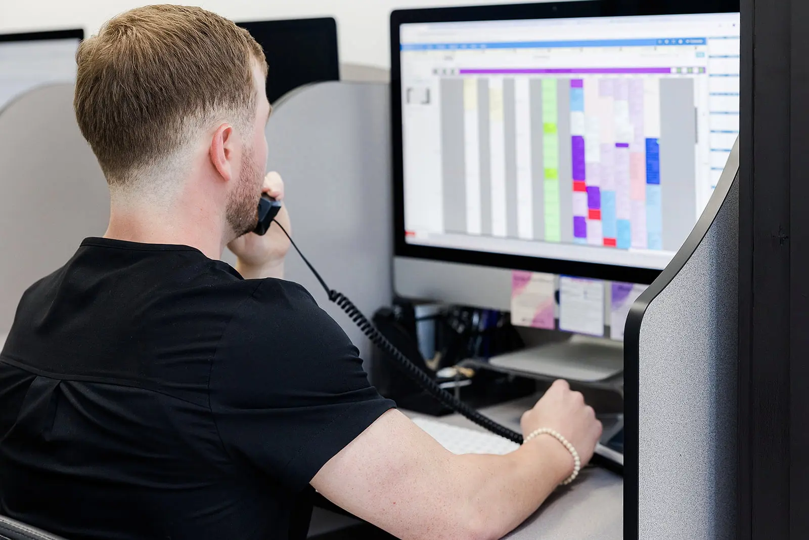 At Redemption Orthodontics in Tallahassee, FL, a person sits at a desk, viewing a colorful schedule on a monitor while on the phone.