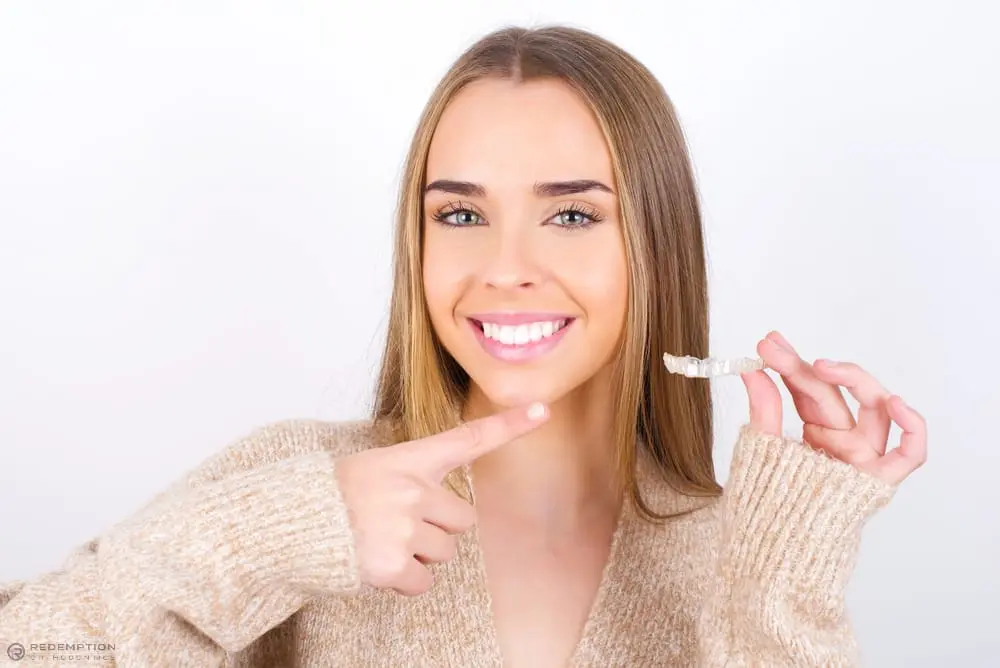 Smiling woman with long hair points to a clear dental aligner at Redemption Orthodontics in Tallahassee, FL - How Does Invisalign Work in Tallahassee, FL
