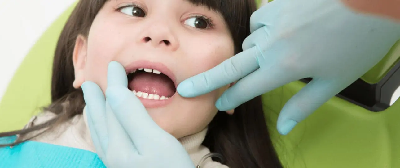 At Redemption Orthodontics in Tallahassee, FL, a dentist in blue gloves examines a child's teeth in the dental chair.