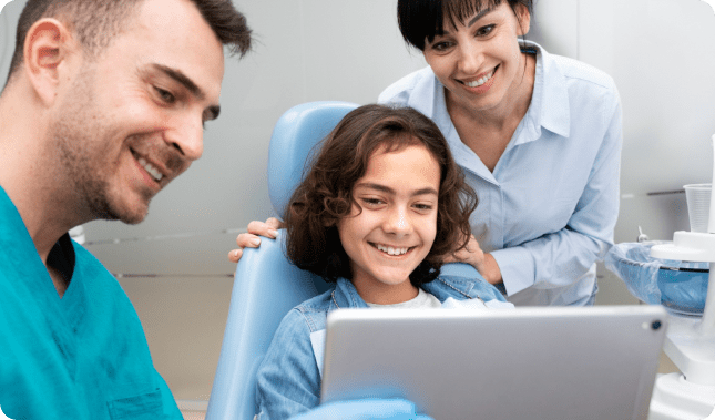 At Redemption Orthodontics in Tallahassee, FL, a child smiles at a tablet held by a dentist as an adult nearby also smiles.
