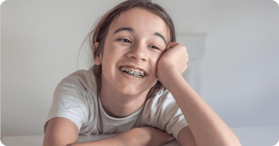 At a white table in Tallahassee, FL, a smiling young person with braces from Redemption Orthodontics rests their head on their hand.