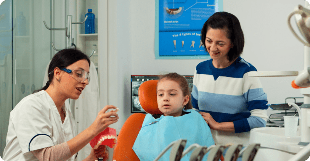 At Redemption Orthodontics in Tallahassee, FL, a dentist discusses dental care with a young girl as her mother stands nearby.