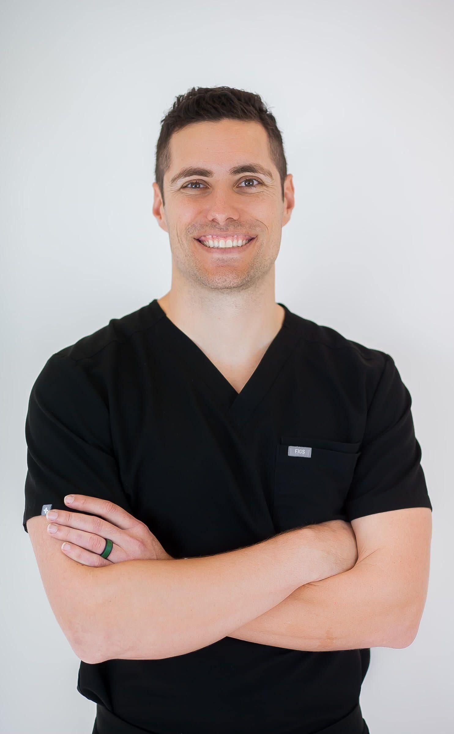 At Redemption Orthodontics in Tallahassee, FL, Dr. Michael Vracar stands confidently in black scrubs with arms crossed and smiling.